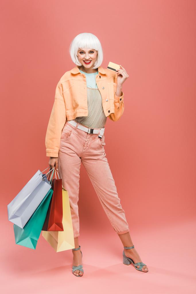 gelukkig meisje in witte pruik met boodschappentassen en creditcard op roze - Foto, afbeelding