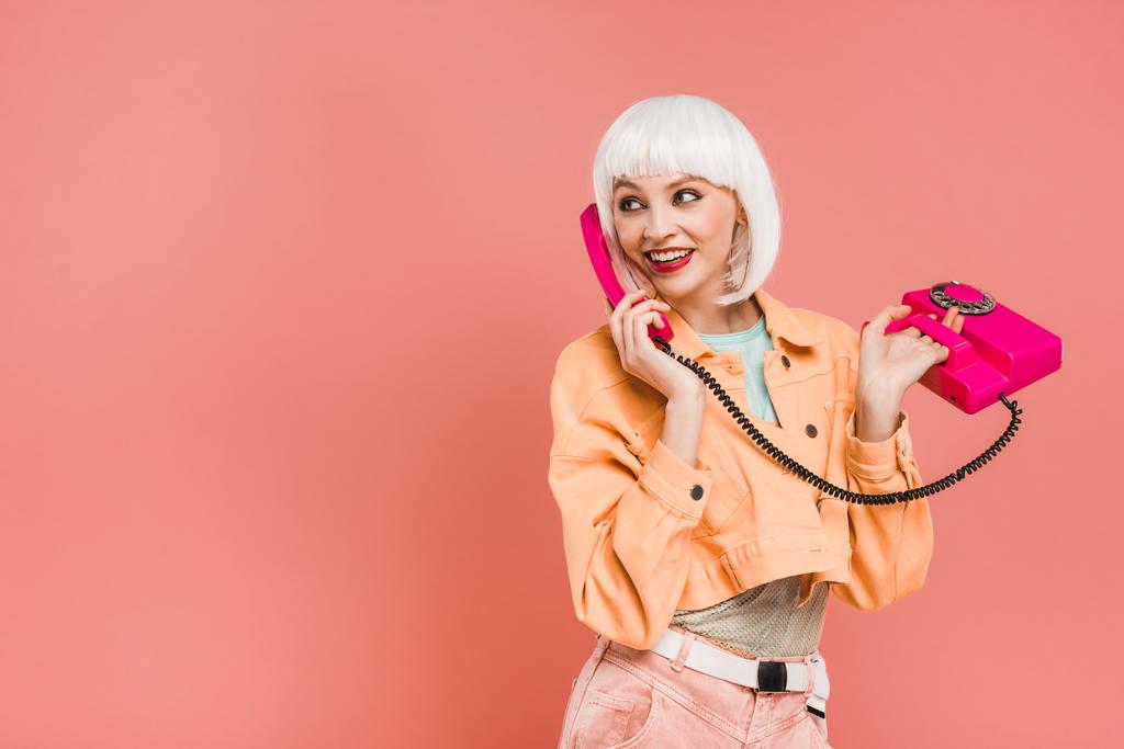 όμορφη νεαρή γυναίκα με λευκό περούκα μιλάει σε ρετρό τηλέφωνο, απομονώνονται σε ροζ  - Φωτογραφία, εικόνα