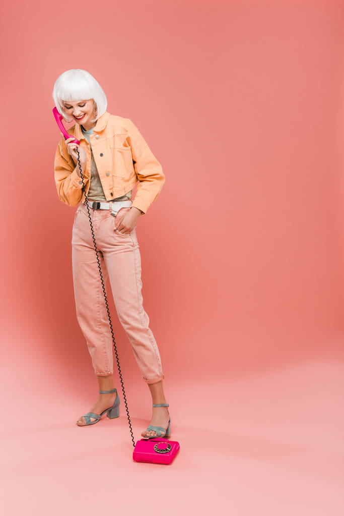 ピンクのヴィンテージ電話で話す白いかつらで美しいファッショナブルな女性  - 写真・画像