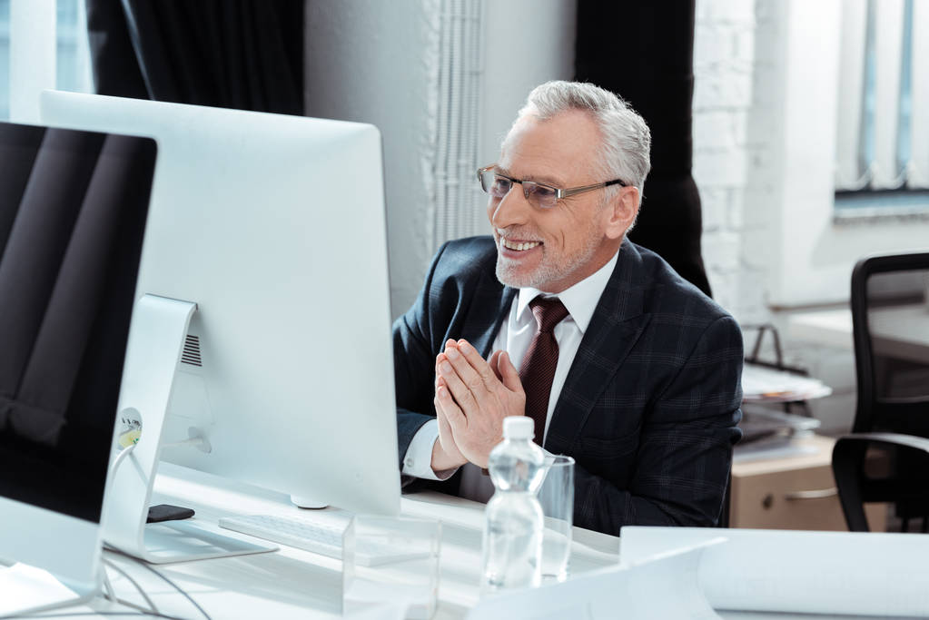 foco seletivo de empresário feliz em óculos gesticulando perto do monitor de computador no escritório moderno
  - Foto, Imagem
