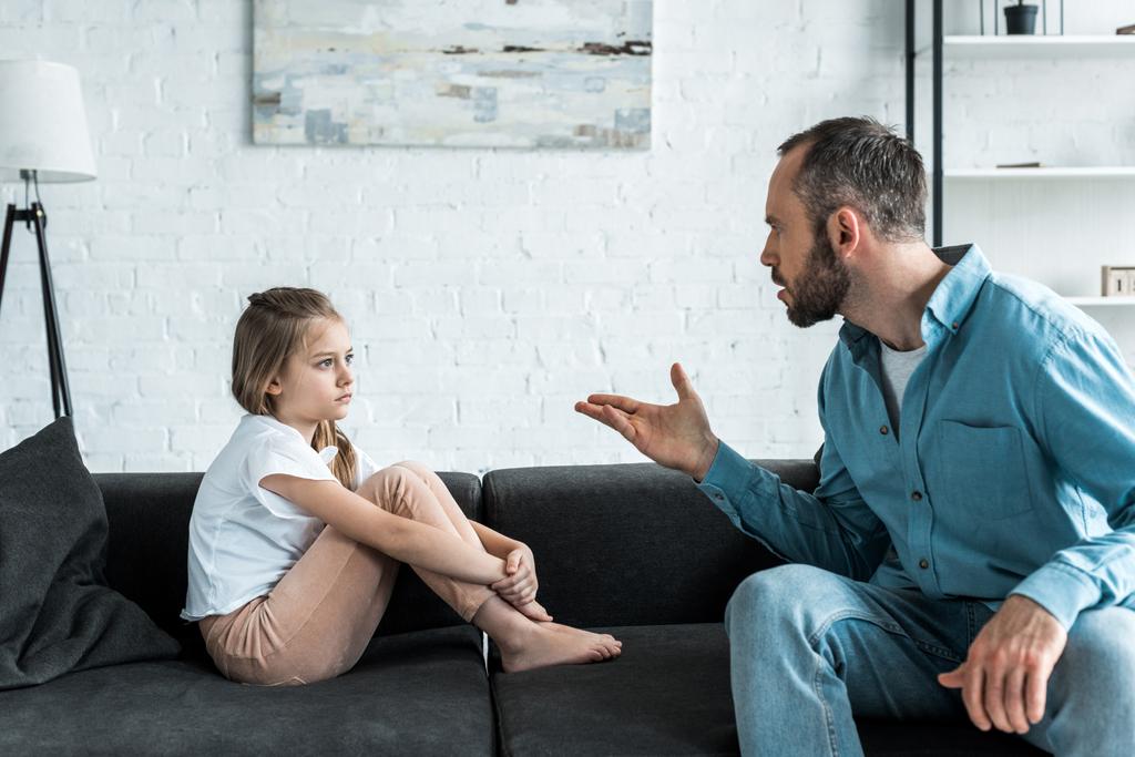enojado padre gesto cerca molesto niño sentado en sofá
  - Foto, imagen