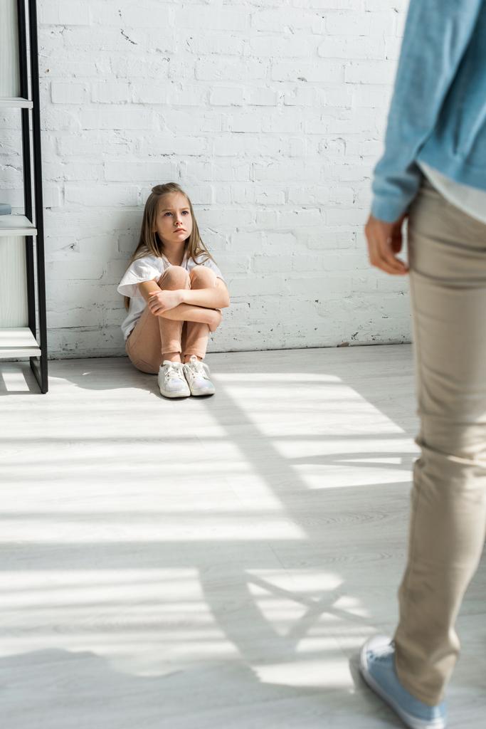 selective focus of upset kid sitting on floor and looking at mother - Photo, Image