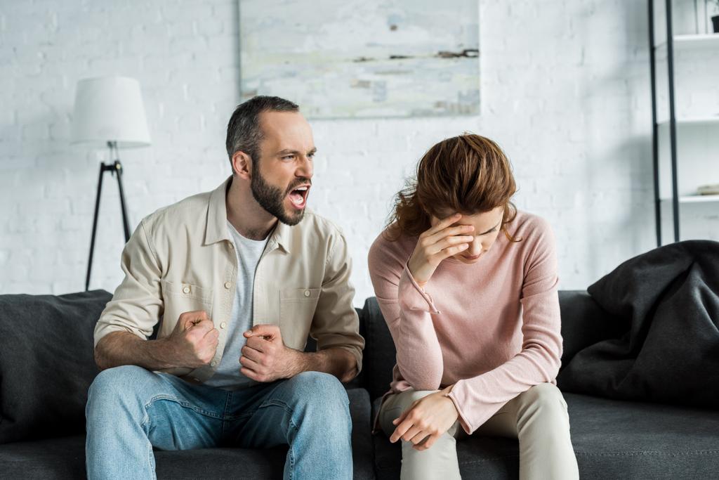 Rozzlobený muž sedí na pohovce a křičí na rozhněvaný ženu  - Fotografie, Obrázek