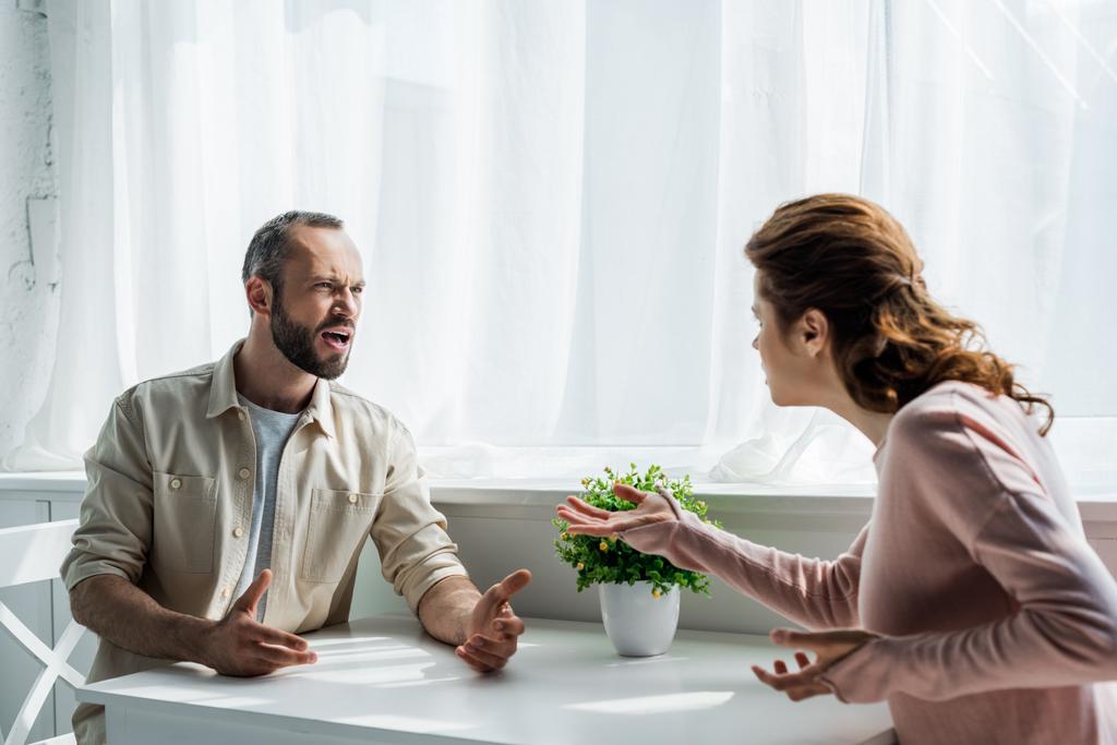 вибірковий фокус сердитого чоловіка жестикулює і дивиться на жінку, сидячи вдома
  - Фото, зображення