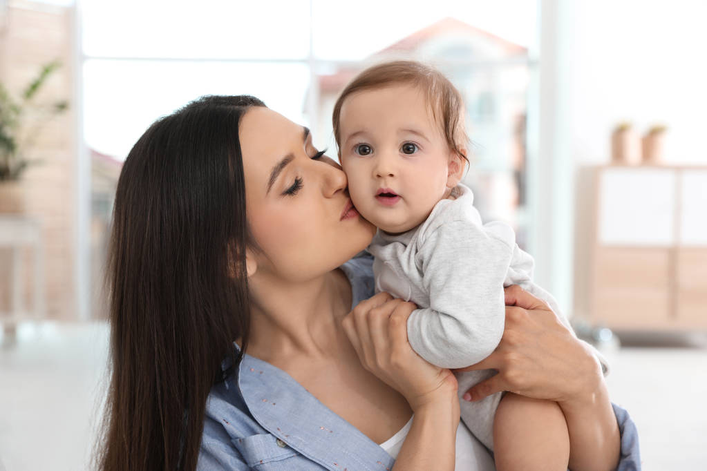 Felice giovane madre baciare il suo adorabile bambino in soggiorno
 - Foto, immagini