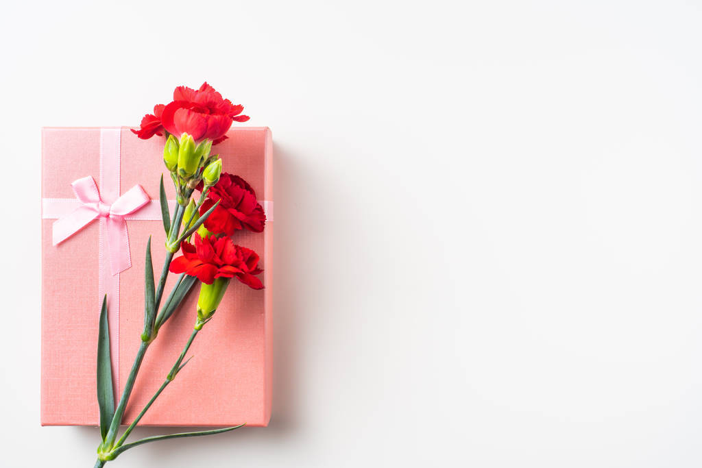Μπουκέτο από κόκκινα γαρίφαλα και κουτί δώρου στο παρασκήνιο με χώρο αντιγραφής - Φωτογραφία, εικόνα