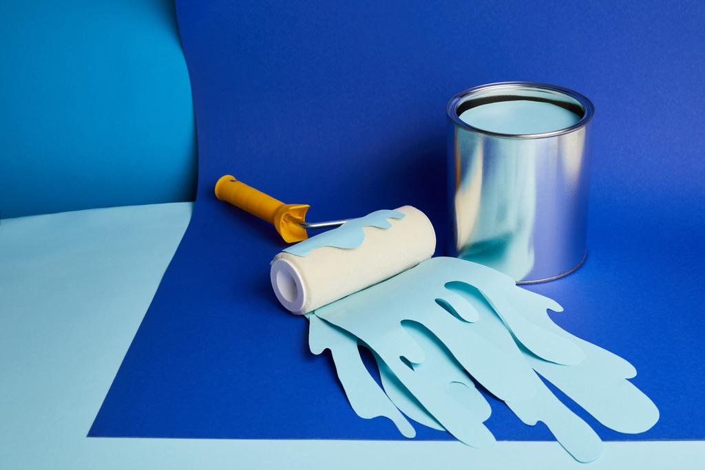 Metalldose und Walze mit tropfender Papierschnittfarbe auf hellblauem Hintergrund - Foto, Bild