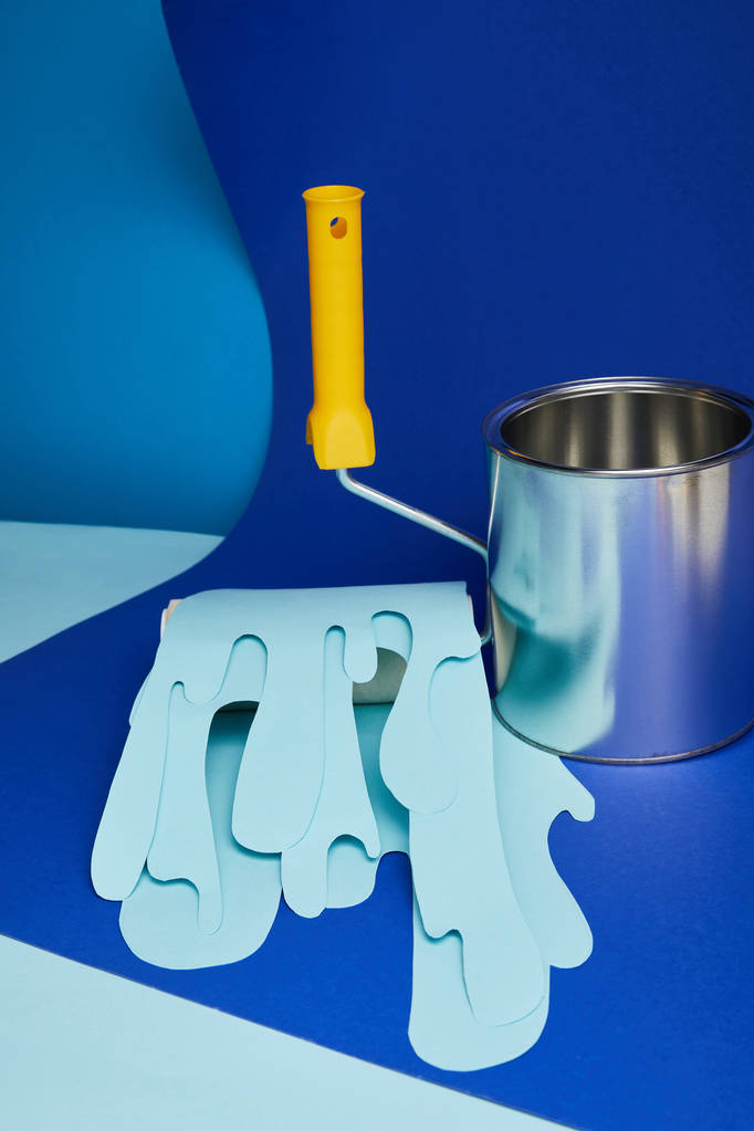boîte brillante en métal près du rouleau avec papier goutte à goutte peinture coupée sur fond bleu vif
 - Photo, image
