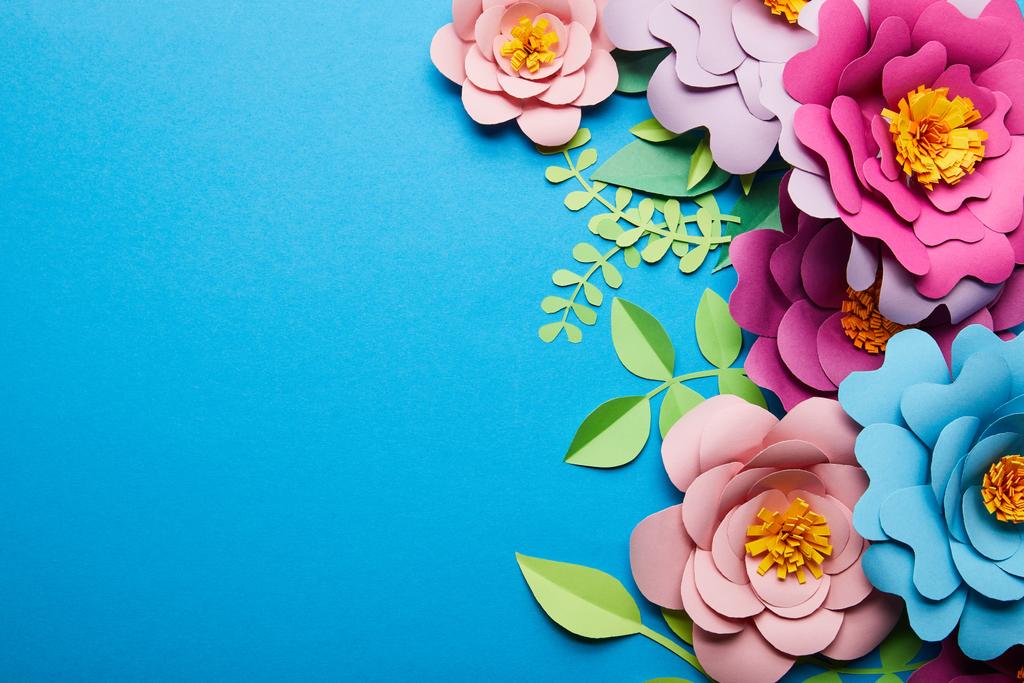 κορυφή θέα του πολύχρωμο χαρτί κομμένα λουλούδια με πράσινα φύλλα σε μπλε φόντο με χώρο αντιγραφής - Φωτογραφία, εικόνα