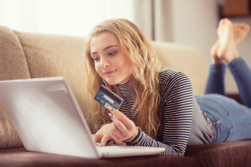 Hermosa joven sosteniendo tarjeta de crédito comprar en línea en el sofá i
 - Foto, imagen