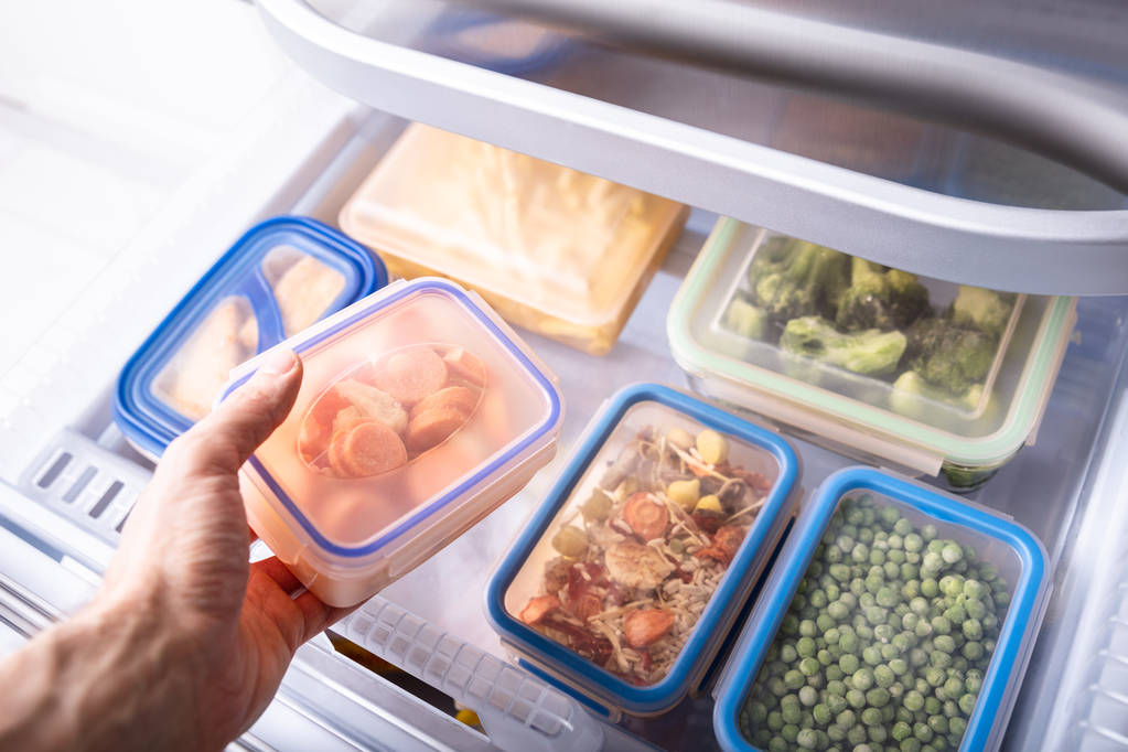 Az ember keze vesz konténer fagyasztott vegyes zöldségek a hűtőszekrényből - Fotó, kép