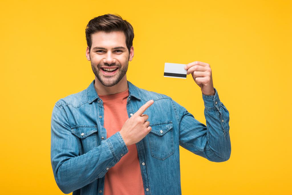 komea mies osoittaa sormella luottokorttia eristetty keltainen
 - Valokuva, kuva