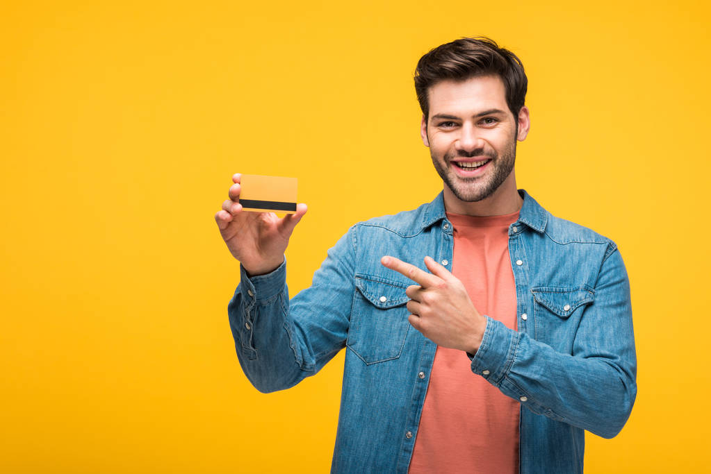 sarı izole kredi kartı parmağı ile işaret mutlu yakışıklı adam - Fotoğraf, Görsel