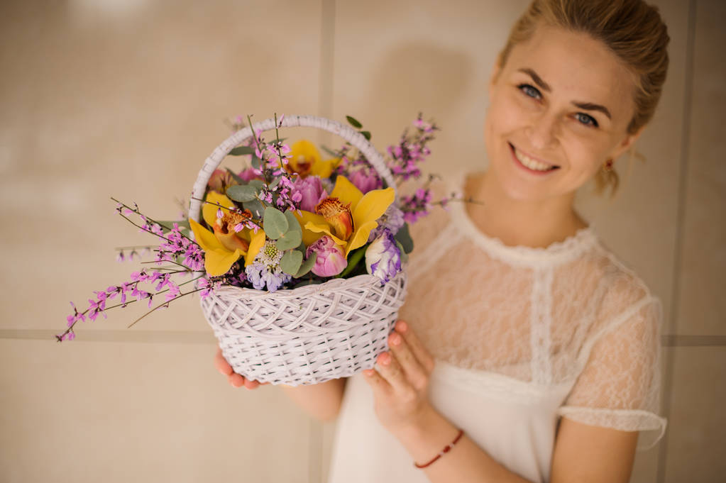 Mulher sorri e segura cesta pequena com flores
 - Foto, Imagem