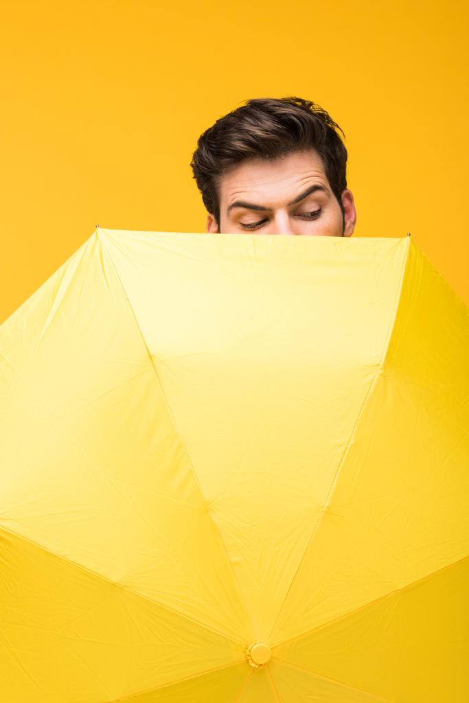 傘で顔を覆い、黄色で孤立した下を見下ろすハンサムな男 - 写真・画像