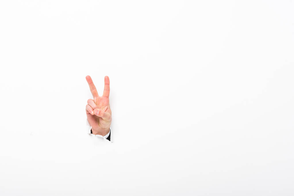 homem mostrando sinal de paz do buraco na parede de papel no branco com espaço de cópia
 - Foto, Imagem