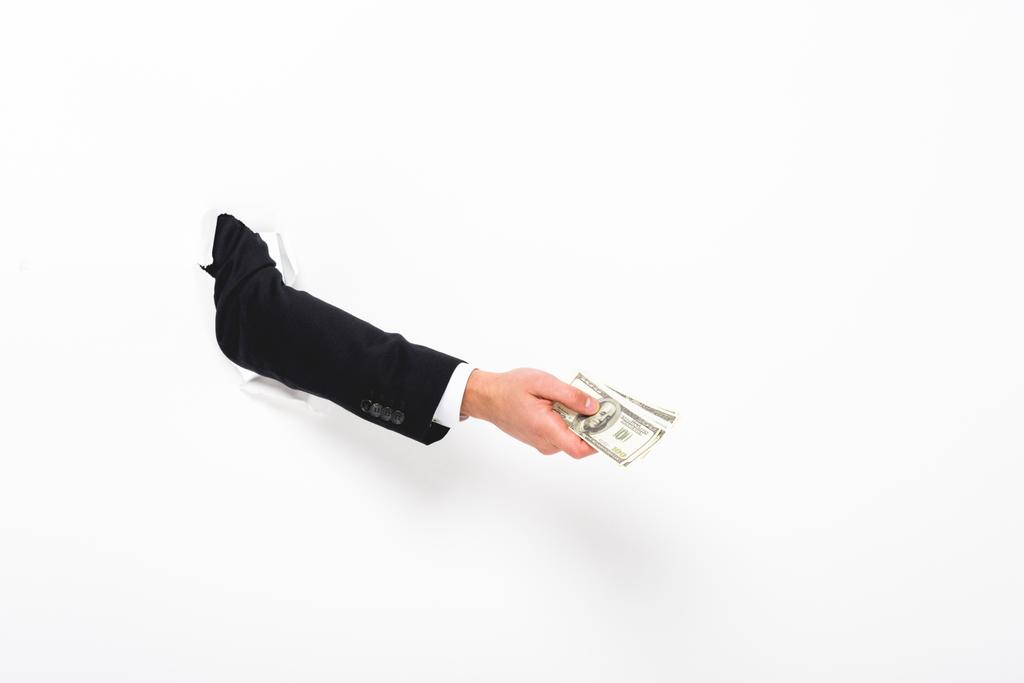 Περικομμένη όψη του ανθρώπου που κρατά τα χρήματα μέσα από την τρύπα σε χαρτί τοίχου σε λευκό - Φωτογραφία, εικόνα