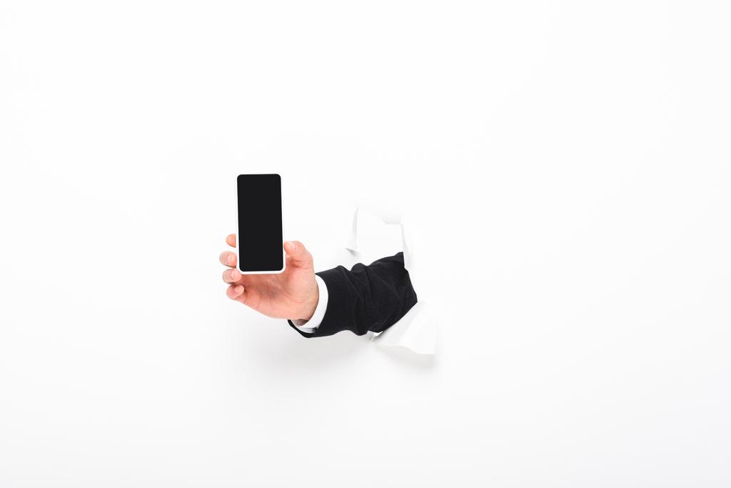 Oříznutý pohled člověka, který drží smartphone od otvoru ve zdi na bílém s prostorem pro kopírování - Fotografie, Obrázek