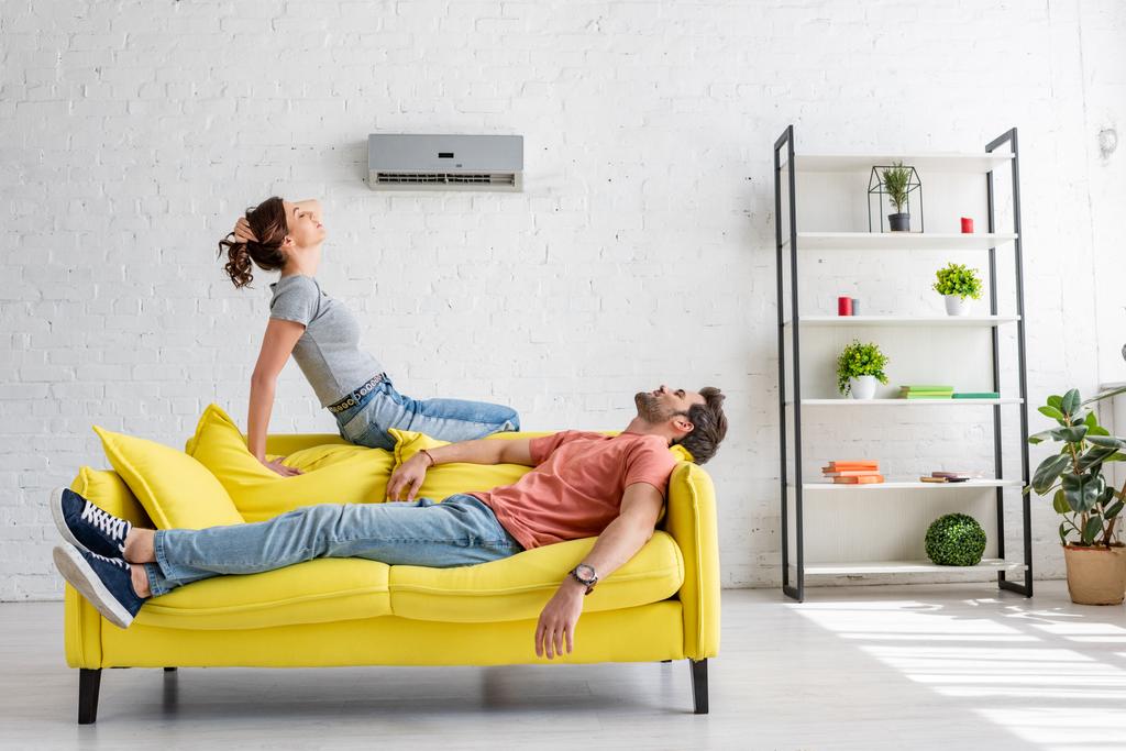 joven hombre y mujer descansando en el sofá amarillo bajo el aire acondicionado en casa
 - Foto, Imagen