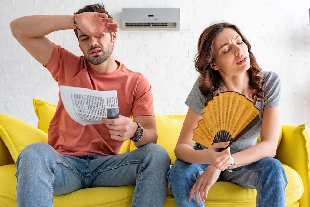 exhausted man and woman sitting on sofa and suffering from heat at home - Photo, Image