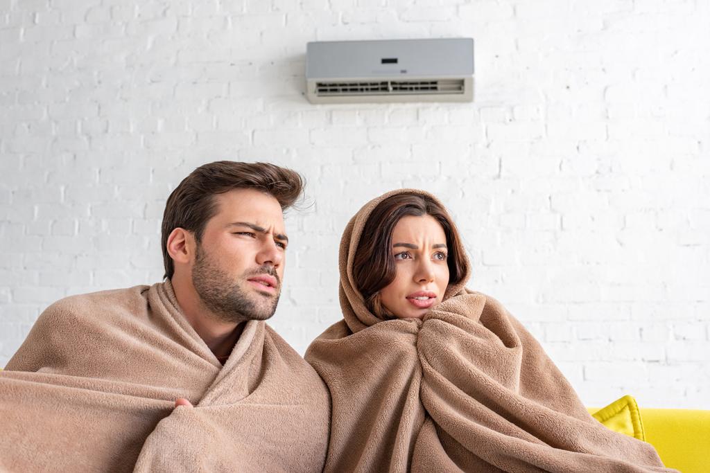 fagyasztott férfi és nő felmelegedés alatt takaró alatt ülve klímaberendezés  - Fotó, kép