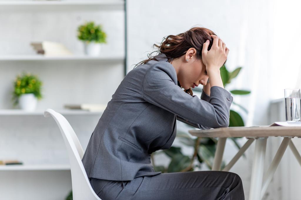mulher de negócios exausta de mãos dadas perto da cabeça enquanto sofre de cabeça no escritório
 - Foto, Imagem