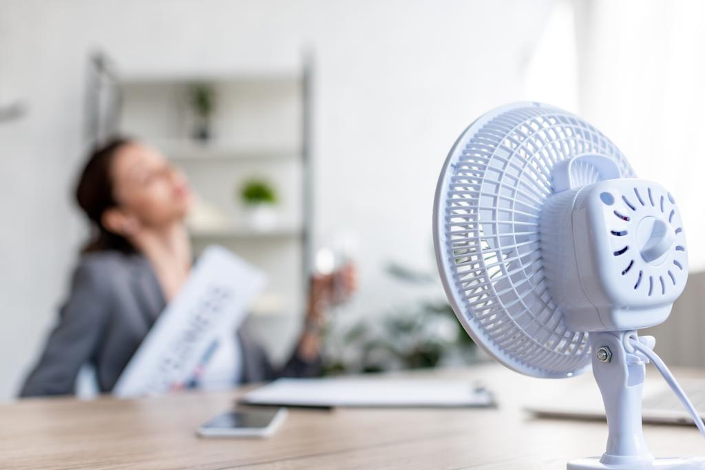 enfoque selectivo de la mujer de negocios que sufre de calor mientras está sentada cerca de ventilador eléctrico
 - Foto, imagen