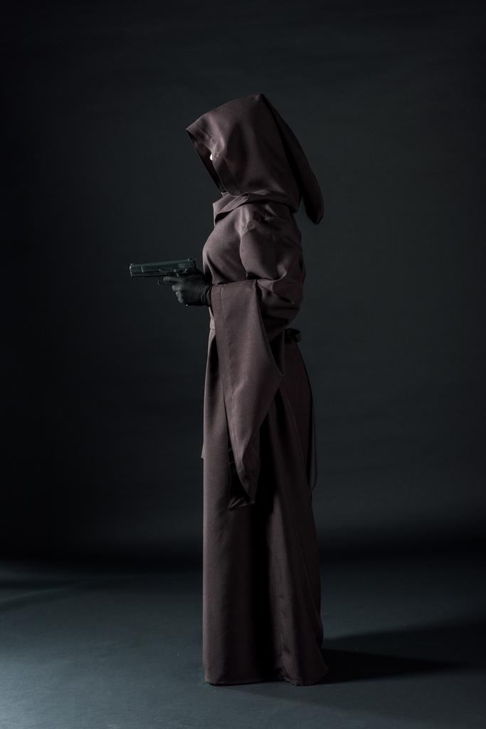 Side όψη της γυναίκας με το θάνατο κοστούμι κρατώντας όπλο σε μαύρο - Φωτογραφία, εικόνα