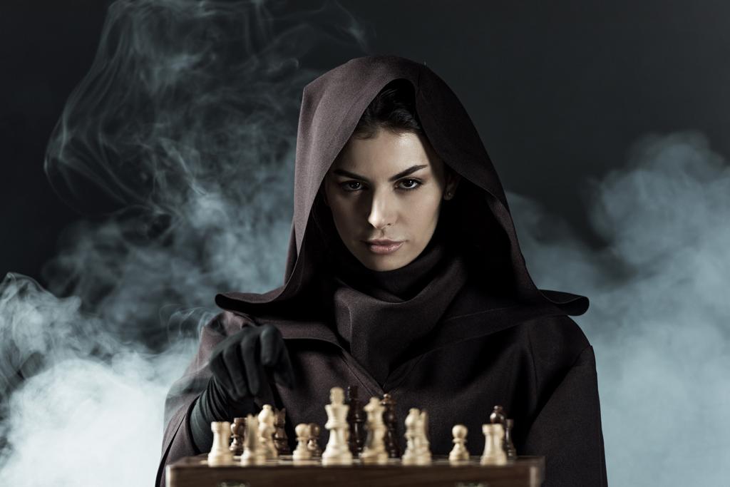 woman in death costume playing chess in smoke on black - Photo, Image