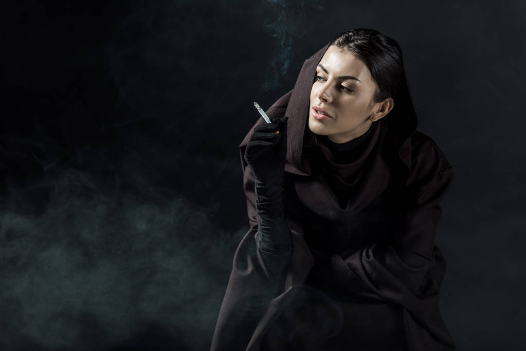 vrouw in dood kostuum roken sigaret op zwart - Foto, afbeelding
