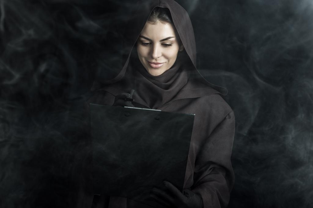 woman in death costume holding clipboard on black - Photo, Image
