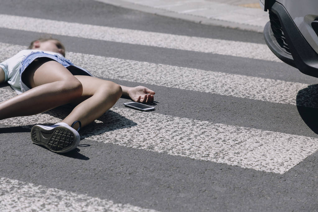 Nastoletni Dziewczyna z telefonem komórkowym leżącego na ulicy po strasznym wypadku samochodowym na przejściu pieszych - Zdjęcie, obraz