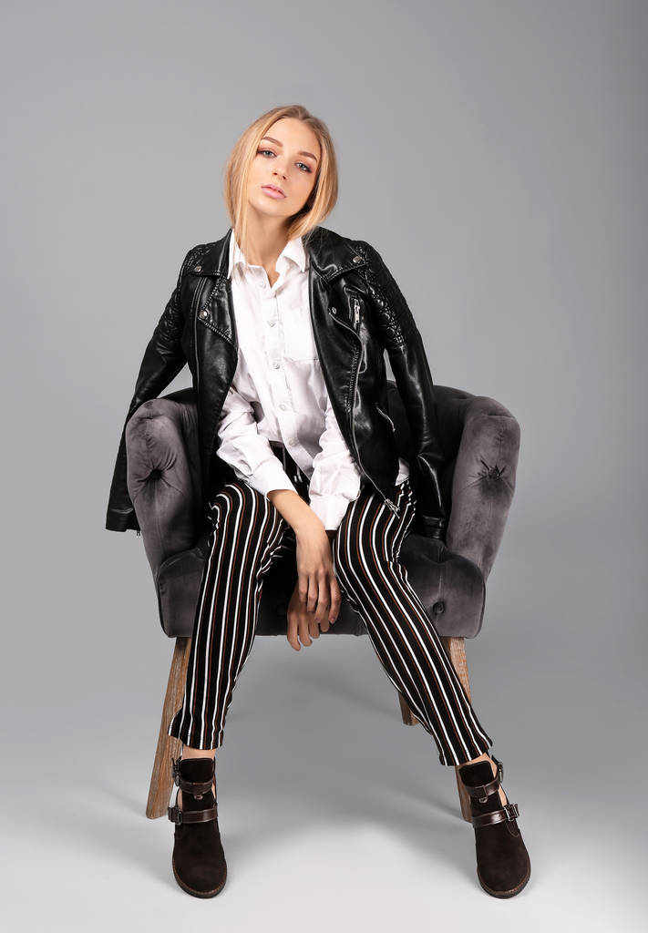 Mujer joven y elegante con zapatos de moda sentados en sillón sobre fondo gris
 - Foto, imagen