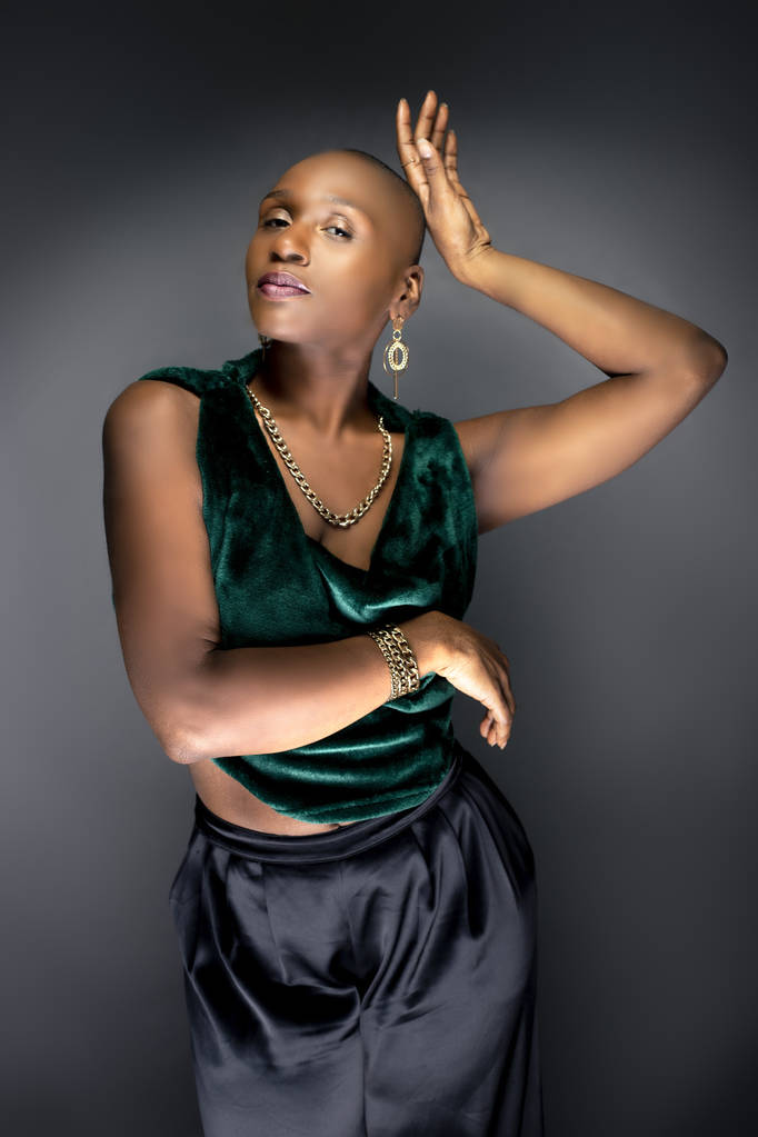 Μαύρο αφρικανικό αμερικανικό θηλυκό μοντέλο που ποζάρει με φαλακρό χτένισμα και πράσινα μοντέρνα ρούχα. Η τολμηρή μοντέρνα εμφάνιση της και το μυϊκό και κατάλληλο σώμα της αντιπροσωπεύουν μια ισχυρή και σίγουρη γυναίκα.   - Φωτογραφία, εικόνα