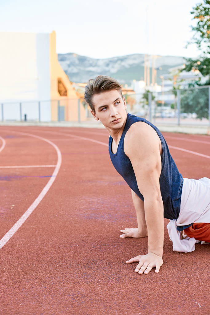 Nuori lihaksikas mies venyttely kilparadalla stadionilla
 - Valokuva, kuva