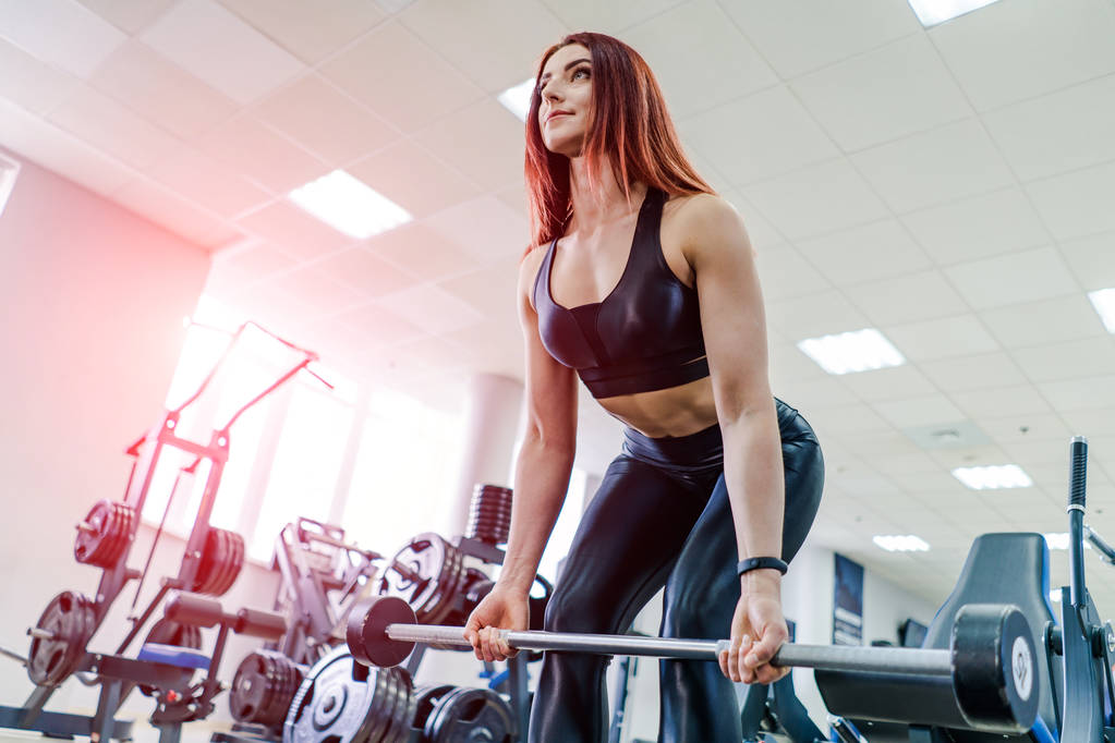 Подходящая молодая женщина, поднимающая штангу, выглядит сосредоточенной, тренируется в спортзале. Молодая и красивая женщина упражнения с штангой
. - Фото, изображение