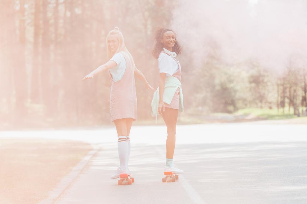 volle Länge Ansicht von zwei Mädchen Skateboarding auf Penny-Boards in Rauch auf der Straße - Foto, Bild