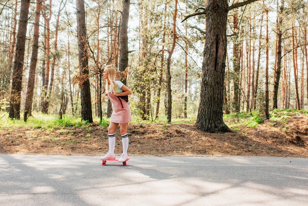 volledige lengte weergave van blonde meisje in knie sokken skateboarden op de weg - Foto, afbeelding