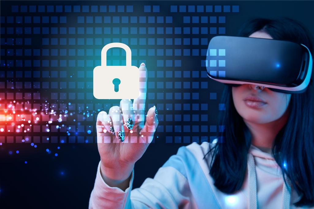 Selektiver Fokus einer jungen Frau im Virtual-Reality-Headset, die mit dem Finger auf glühende Cyber-Security-Illustration auf dunklem Hintergrund zeigt - Foto, Bild