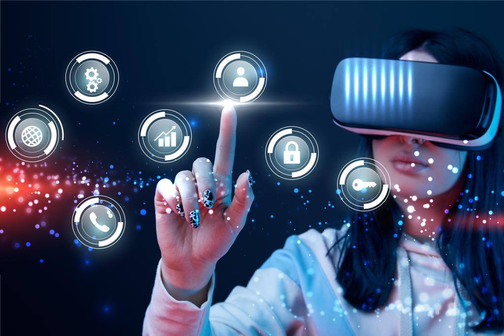 selectieve focus van jonge vrouw in Virtual Reality headset wijzend met vinger op gloeiende Cyber iconen op donkere achtergrond - Foto, afbeelding