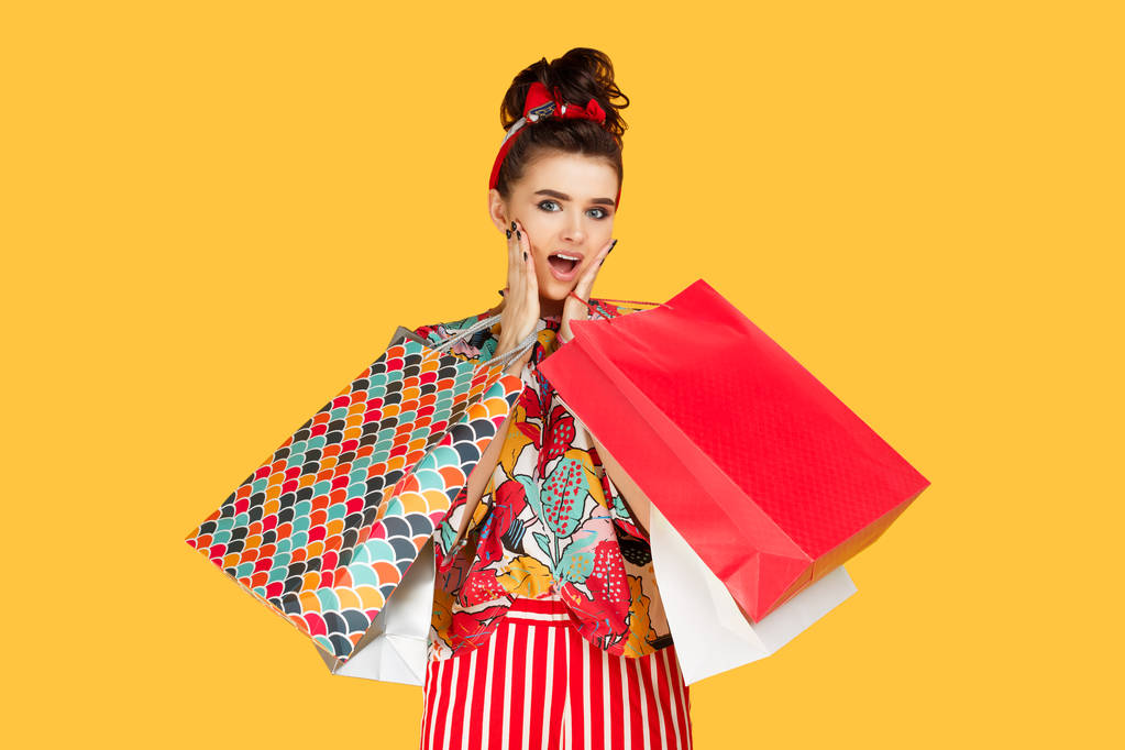 schockierte junge kaukasische Frau in lässiger bunter Kleidung mit Taschen und Einkäufen vor orangefarbenem Hintergrund. Einkaufs- und Vertriebskonzept. - Foto, Bild