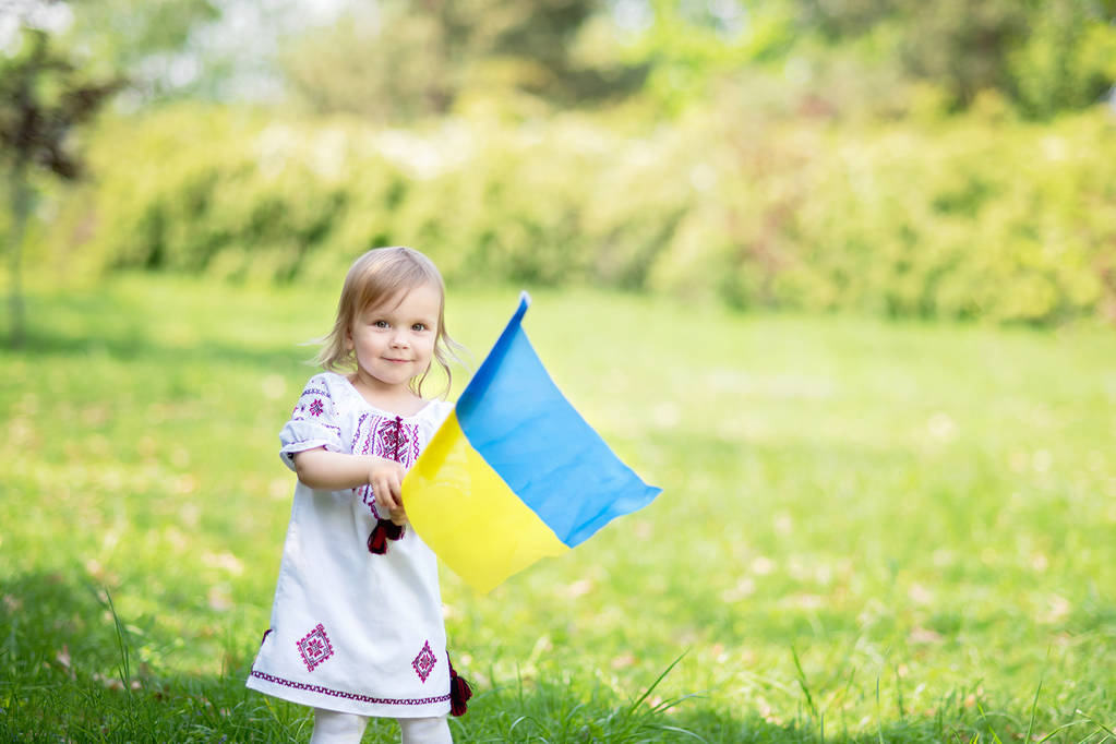 Dziecko nosi trzepoczącą niebiesko-żółtą flagę Ukrainy na polu. Dzień Niepodległości Ukrainy. Dzień Flagi. Dzień Konstytucji. Dziewczyna w tradycyjnym hafcie z flagą Ukrainy. - Zdjęcie, obraz