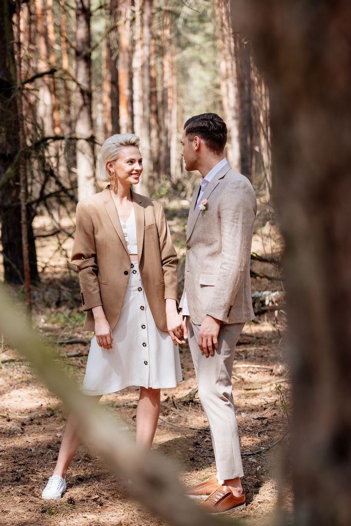 Selective focus of handsome man and attractive woman holding hands in forest - Photo, Image