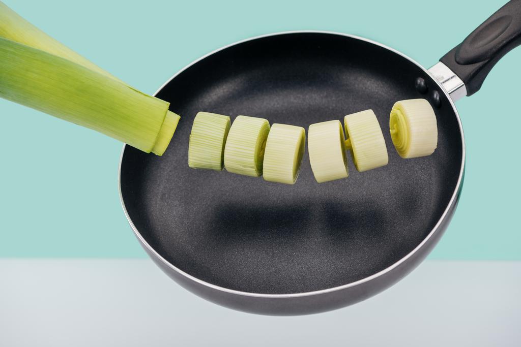 Fresh green leek in frying pan isolated on turquoise - Photo, Image