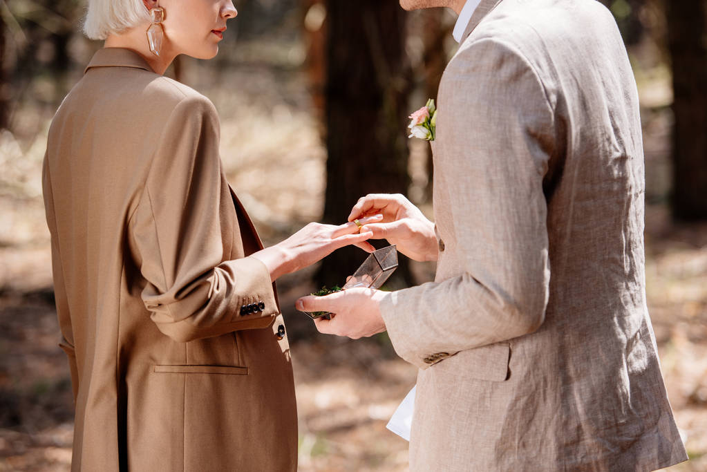 Partial view of man putting on wedding ring on woman finger in forest - Photo, Image