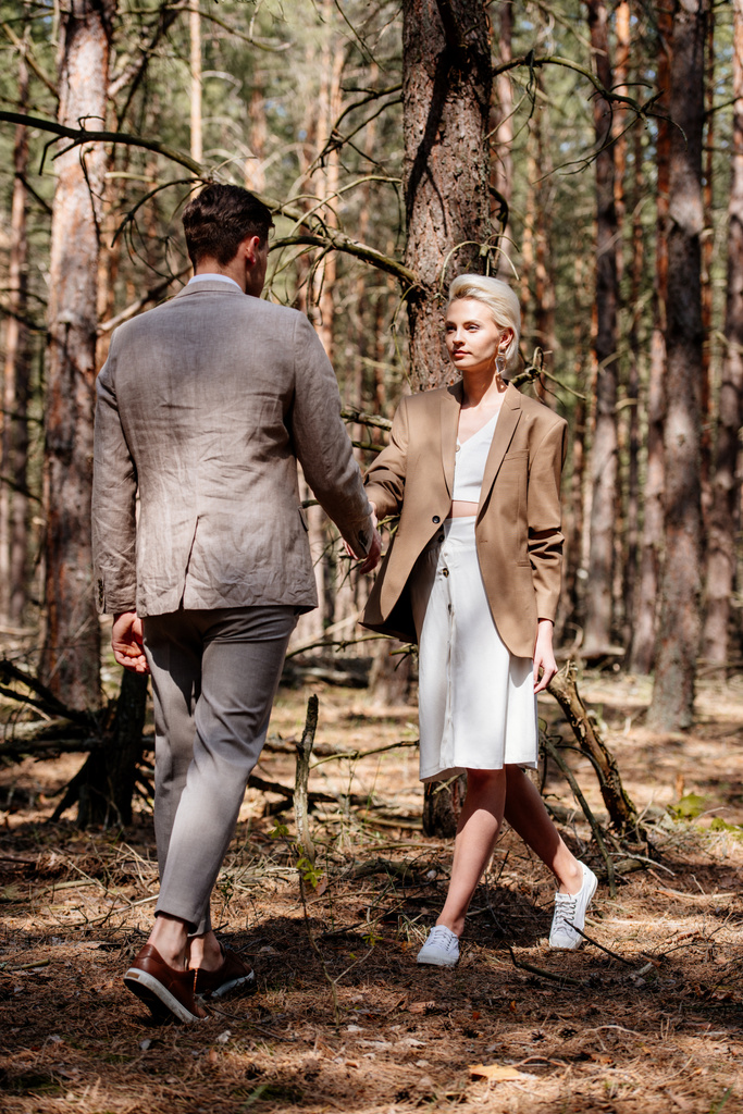 Вид ззаду чоловік і жінка тримають руки один перед одним в лісі
 - Фото, зображення