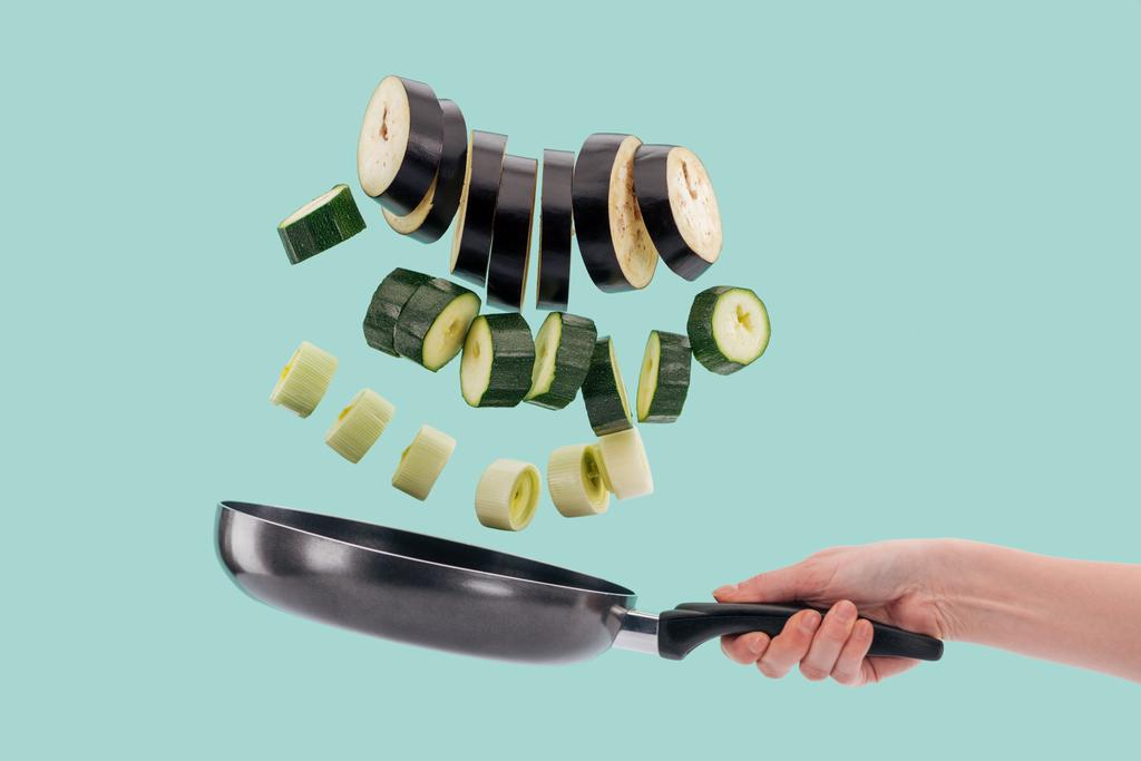 Vue en coupe d'une femme tenant une poêle à frire avec des légumes frais tranchés ci-dessus isolés sur turquoise
  - Photo, image