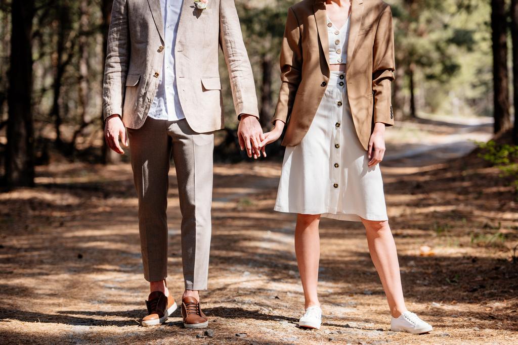 vista ritagliata di coppia alla moda che si tiene per mano nella foresta
 - Foto, immagini