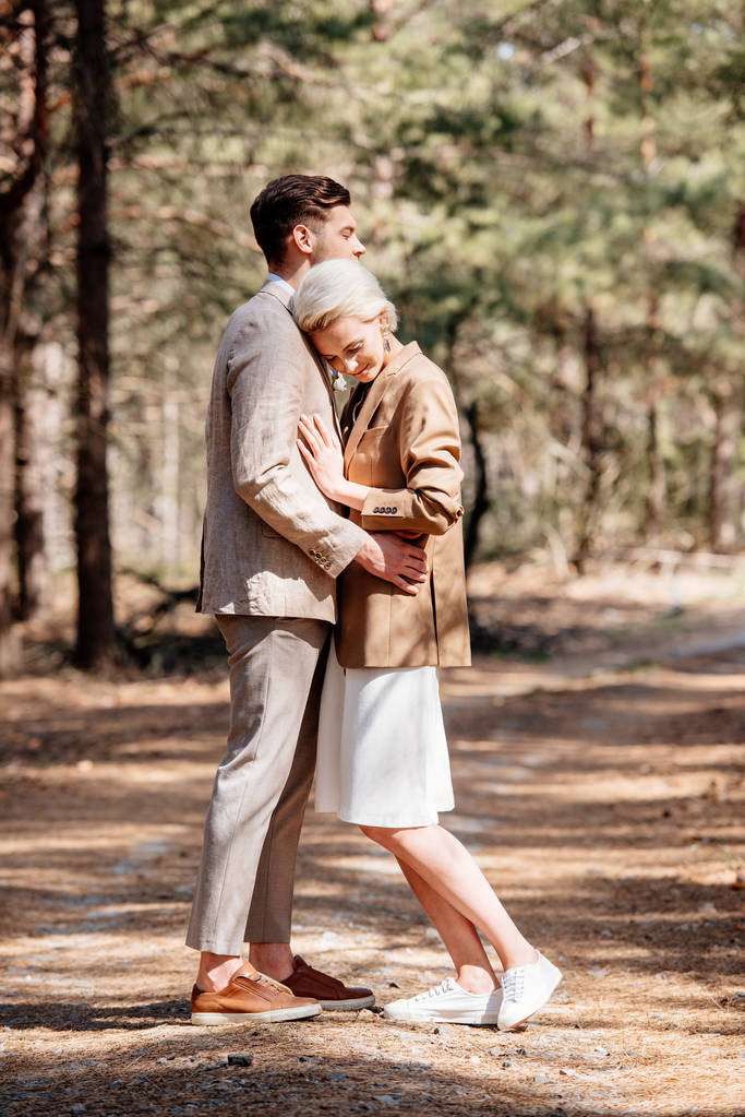 vista completa de pareja con estilo en chaquetas elegantes abrazando en el bosque
 - Foto, imagen