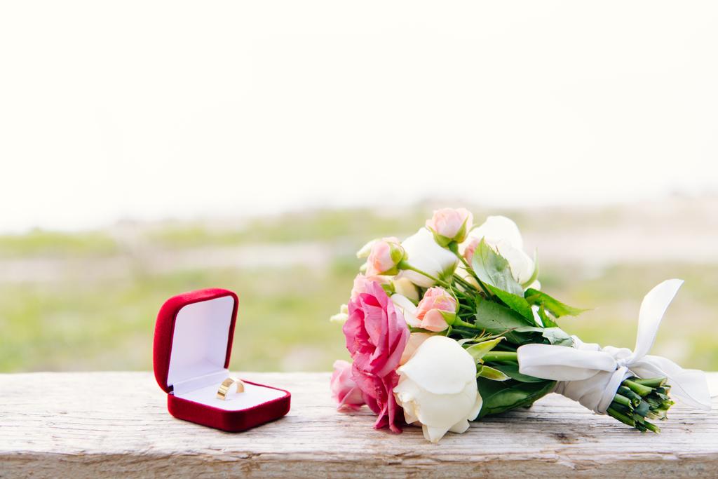 обручальное кольцо в красной коробке и букет на деревянной поверхности
 - Фото, изображение